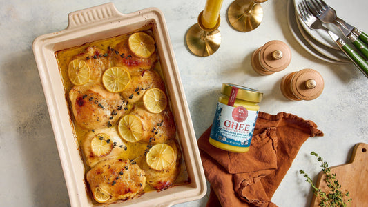 A pink casserole dish filled with Roasted Honey Mustard Chicken next to a jar of 4th & Heart ghee.
