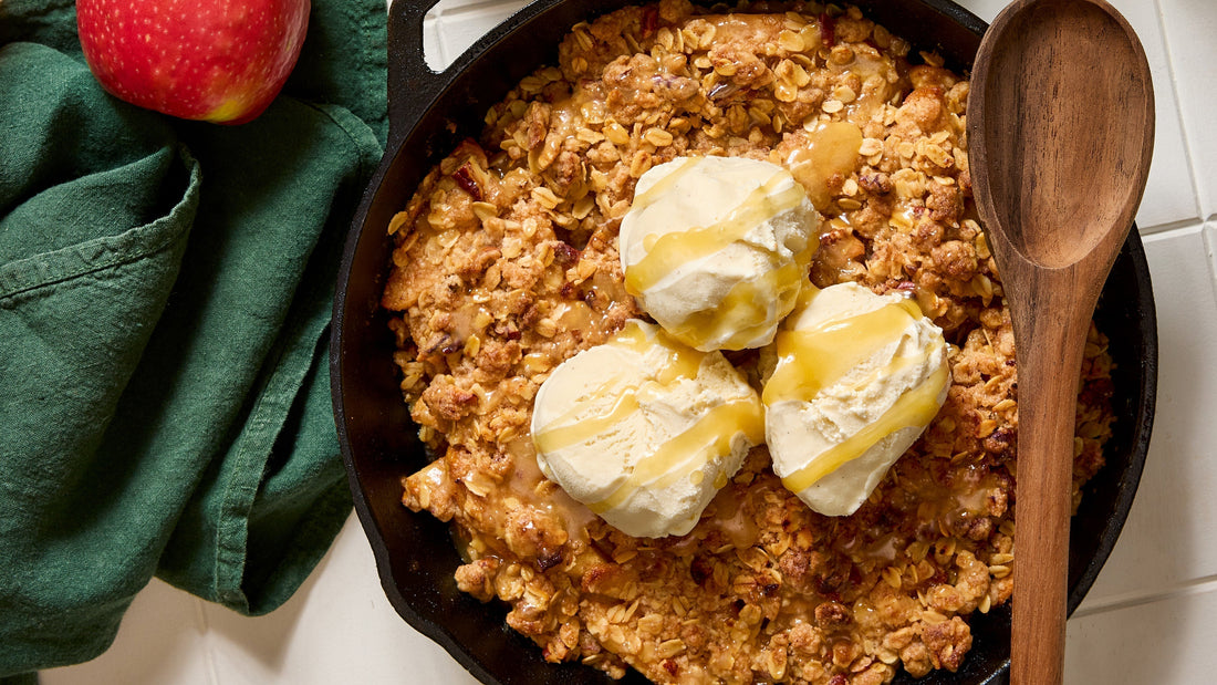 A skillet with Skillet Caramel Apple Crisp and 3 scoops of vanilla ice cream with caramel drizzle on top.