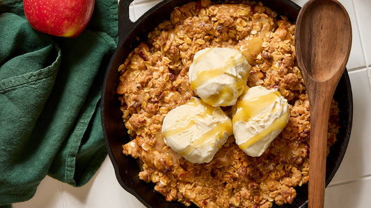 A skillet with Skillet Caramel Apple Crisp and 3 scoops of vanilla ice cream with caramel drizzle on top.