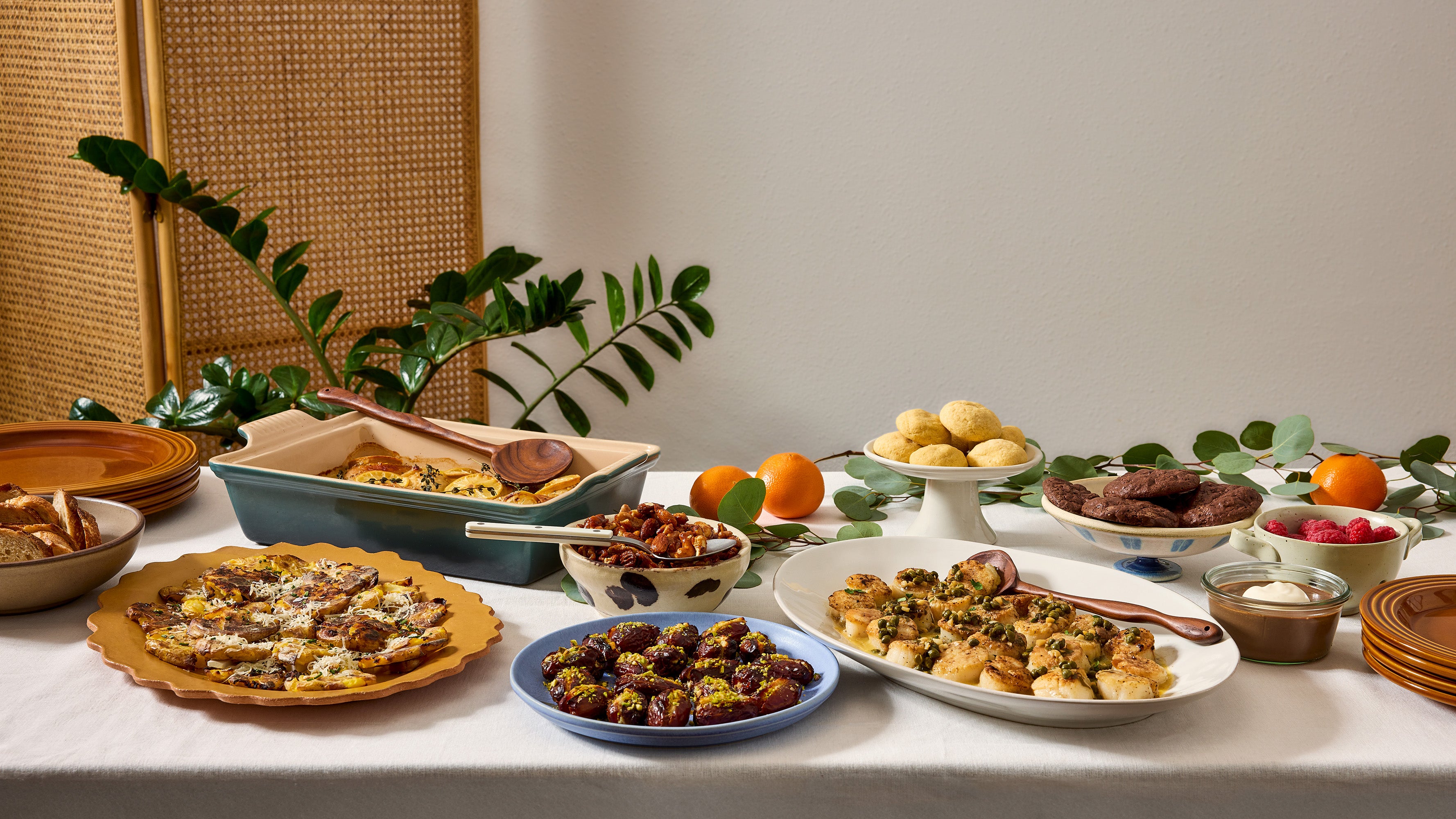 Table with various dishes of food on a white tablecloth, with a neutral background.
